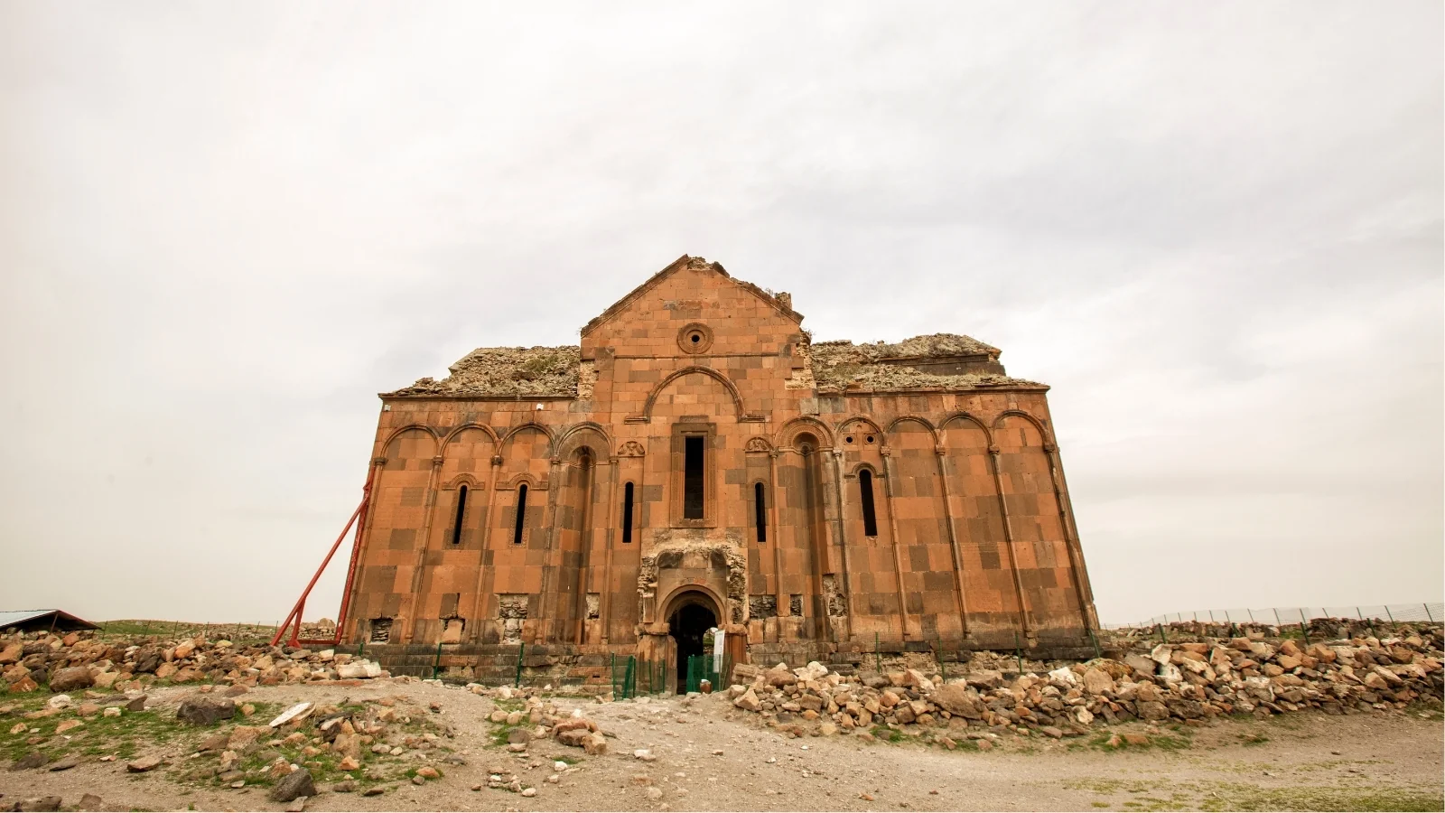 The reddish stone facade of Ani cathedral on the plateau by the Armenian border under an overcast sky